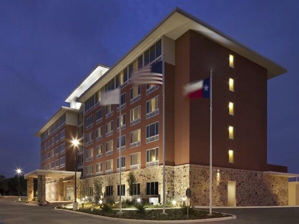 A multi-story hotel with a stone facade, multiple windows, and a flagpole with the Texas flag.
