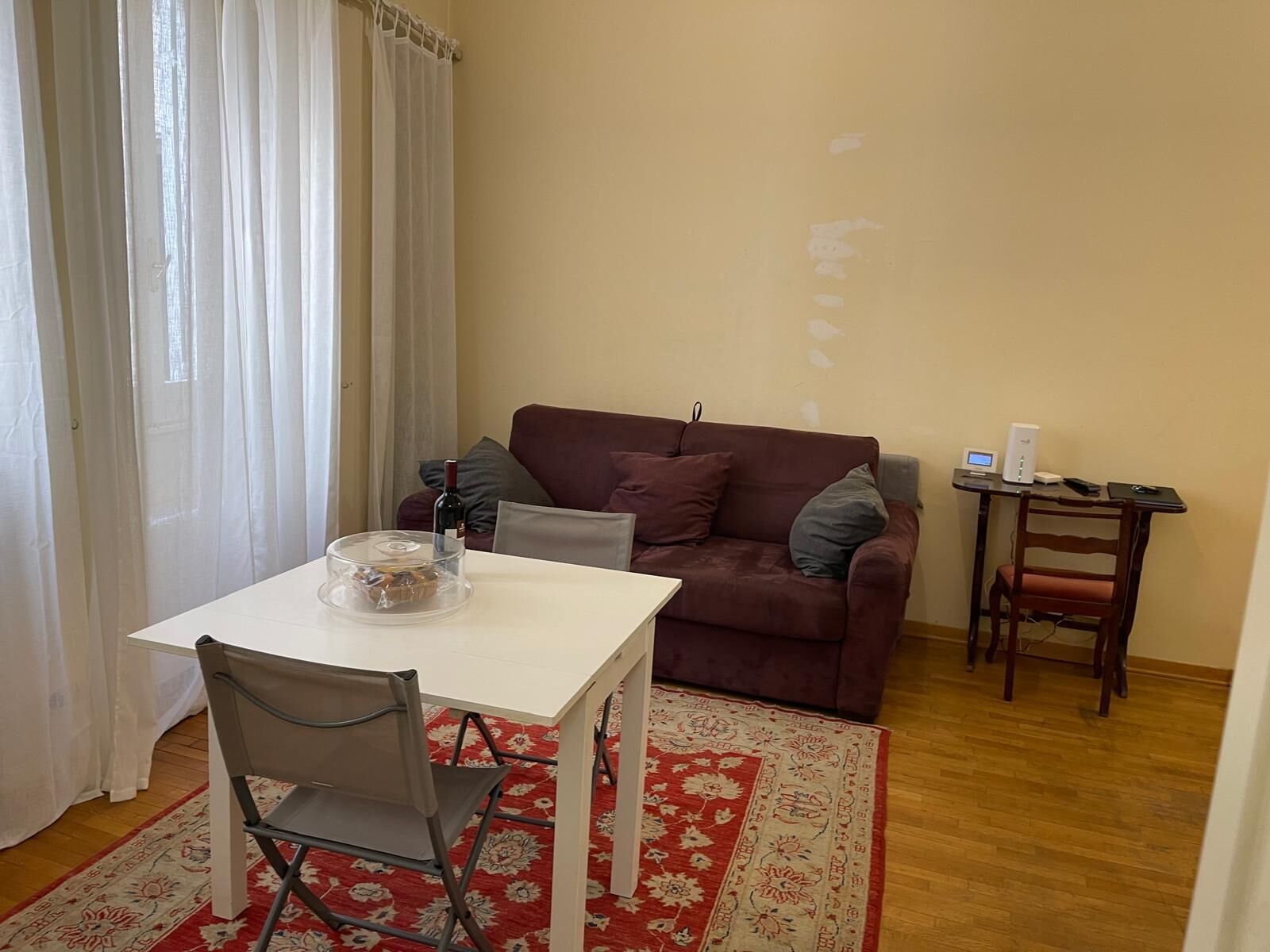 A small living area with a white table, a red and white rug, a brown sofa, and a small side table with a computer and a chair.