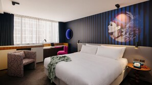 Ein Hotelzimmer mit einem Bett, einem Schreibtisch, einem Stuhl, einem Telefon und einer Wand mit Wandgemälde.