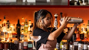 Un barista prepara cocktail dietro un bancone, circondato da bottiglie e bicchieri.