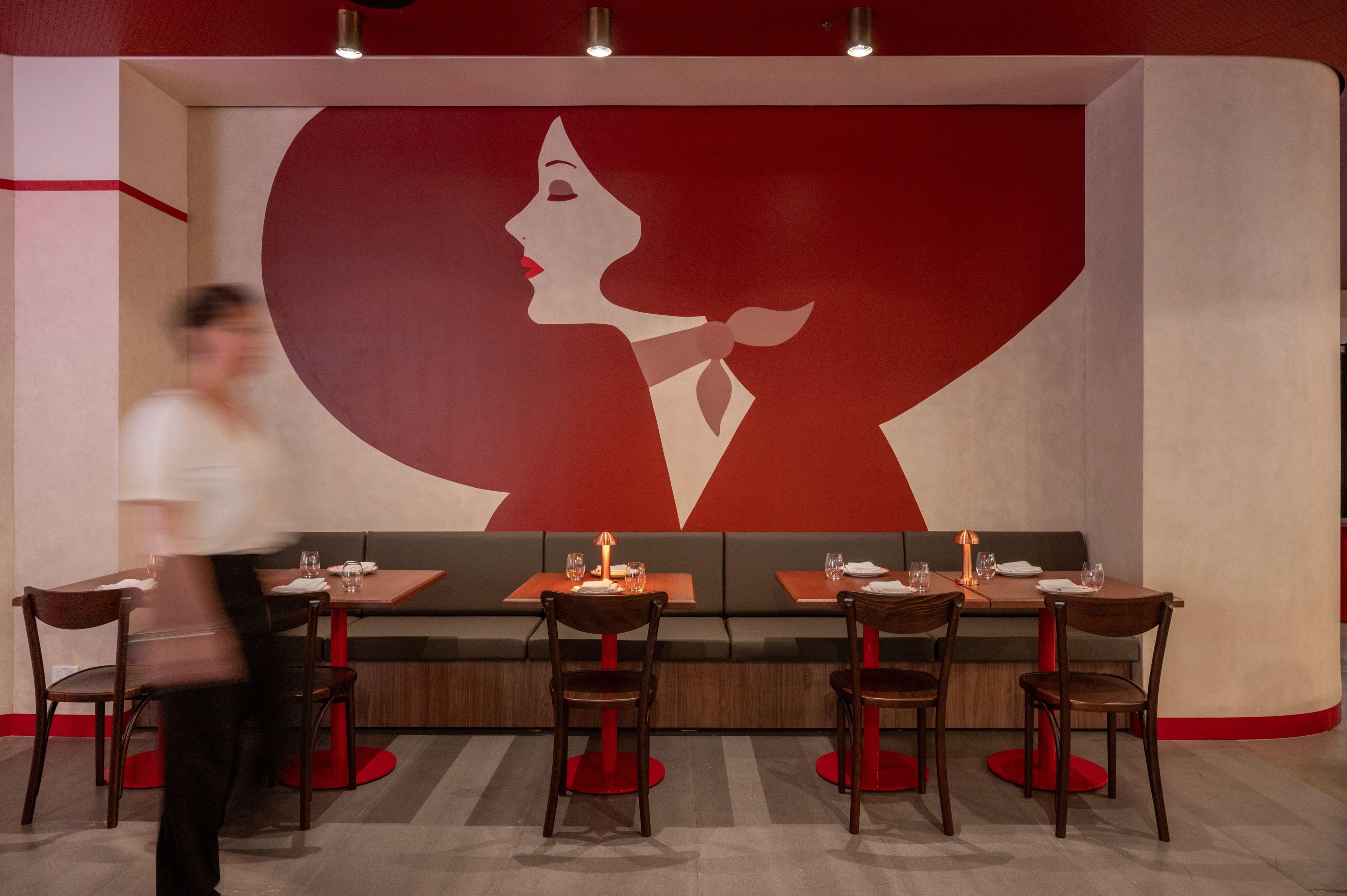 A restaurant with a large wall mural, booths, and tables with chairs.