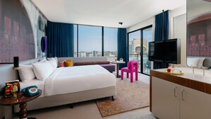 Una camera d'albergo con un letto, una scrivania, una TV, un balcone con vista e un'ampia finestra.