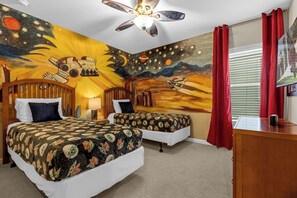 Experience the galaxy in this vibrant room featuring a space-themed mural, two single beds, and a ceiling fan.