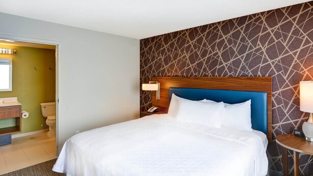 Ein Hotelzimmer mit Bett, Nachttischlampen, einem hölzernen Kopfteil, einem Badezimmer mit Toilette und Waschbecken sowie einer Wand mit Muster.