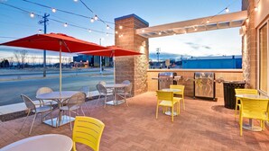 Un'area patio all'aperto con tavoli, sedie, luci decorative a stringa e un barbecue.