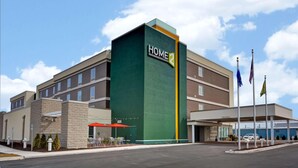 Un hotel a più piani con una facciata verde e beige ben visibile, una zona salotto esterna coperta e diverse bandiere.