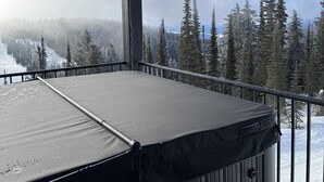 Un balcon doté d’un jacuzzi, offrant une vue sur une forêt enneigée et une montagne.