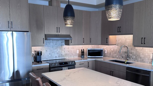 Une cuisine moderne dotée d’appareils électroménagers en acier inoxydable, d’un grand îlot central et de luminaires suspendus.