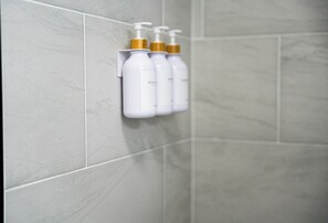 A bathroom with a wall-mounted dispenser holding three bottles of toiletries.