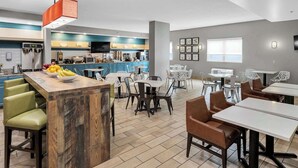 A modern kitchen with a bar area, dining tables, and chairs. - Country Inn & Suites by Radisson, Rehoboth Beach - Dewey (Rehoboth Beach)