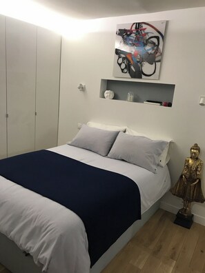 Relax in a serene bedroom with a neatly made bed, a white headboard, and a shelf displaying decorative items.