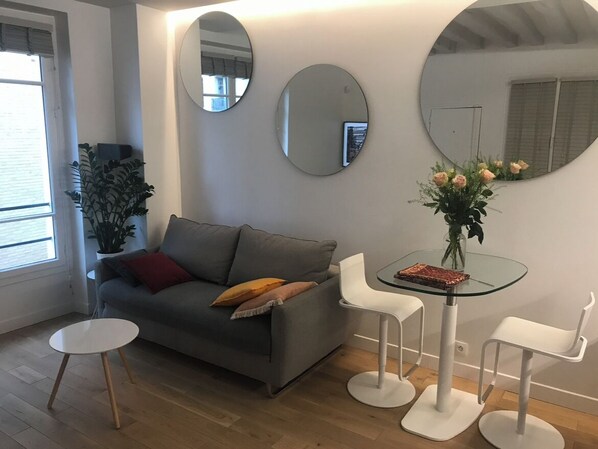 Relax in this stylish living room with a sofa, side table, and coffee table, surrounded by minimalist chairs and mirrors.