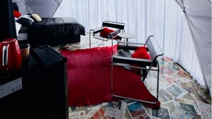 Una habitación con carpa, una cama, un pouf rojo, una mesa y una silla.