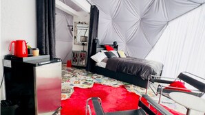 Un dormitorio pequeño con cama, un tapete rojo y mullido, un escritorio y un ventilador de techo.
