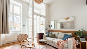 Una sala de estar moderna con un sofá, un sillón mecedora, una mesa redonda y un amplio ventanal con cortinas.