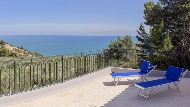 Un balcón con dos sillones azules y barandilla metálica con vistas al paisaje costero.