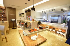 Un restaurante moderno de hotel con una barra de buffet, que incluye una estación de parrilla y una variedad de platos exhibidos en una barra.