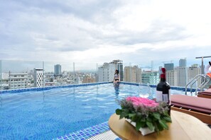 Une piscine sur le toit avec vue sur la ville, une bouteille de vin et un bouquet de fleurs sur une table.