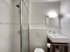 A modern bathroom with a glass shower enclosure, a white sink with a mirror above it, and a toilet with a wooden cabinet.