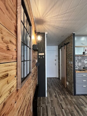 Ein Flur mit Holzwänden, einer schwarzen Tür mit der Aufschrift 'HOME' und einer Küchenzeile mit gemusterten Fliesen.