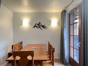Uma área de refeições com mesa e cadeiras de madeira, duas luminárias fixadas na parede e um painel decorativo com tema de montanha.