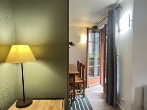 A room with a lamp, a wooden dining table, chairs, a patterned rug, and a door leading to a balcony.