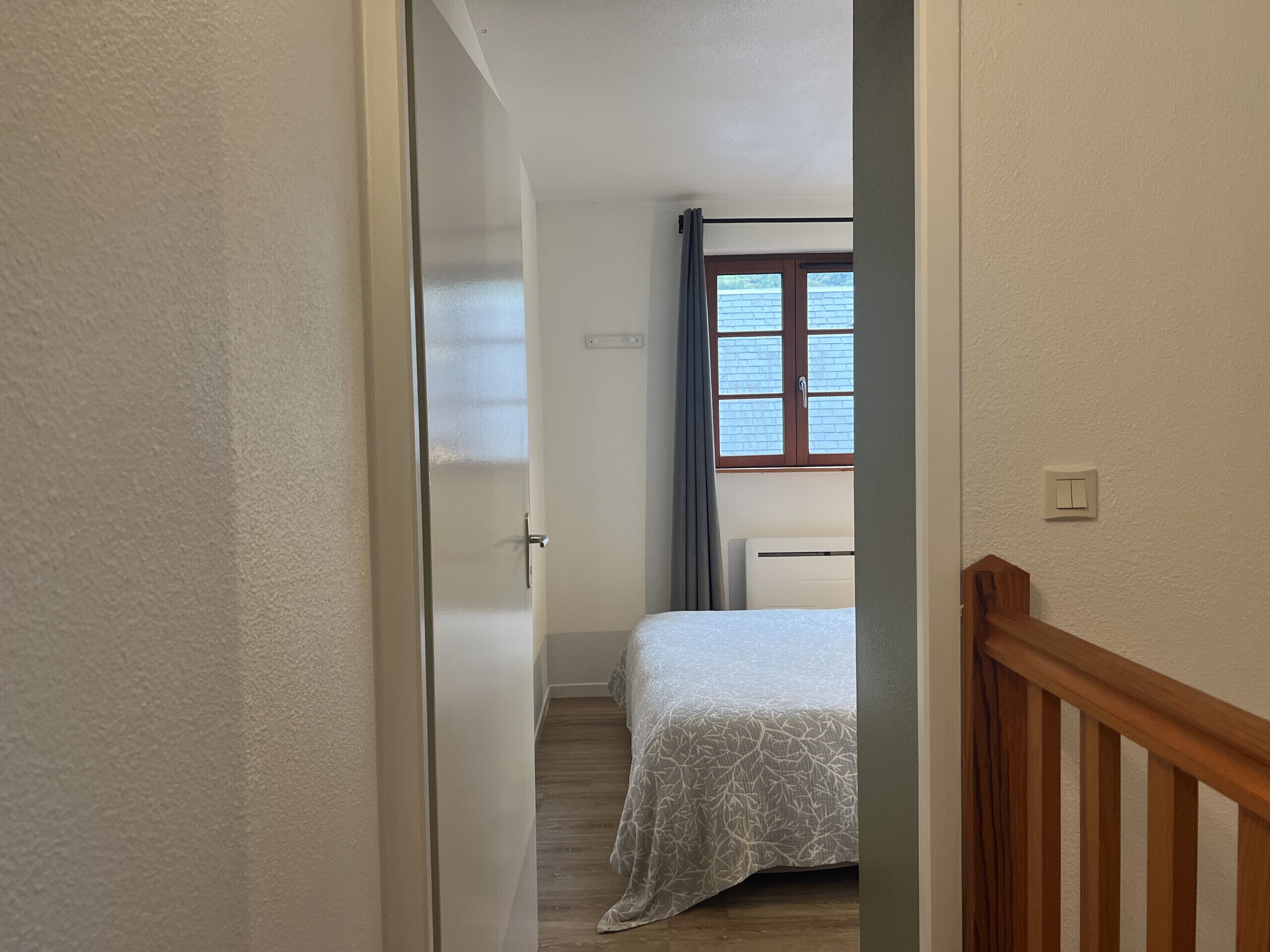 Un couloir étroit mène à une chambre dotée d’une fenêtre, d’une porte et d’un interrupteur sur le mur.