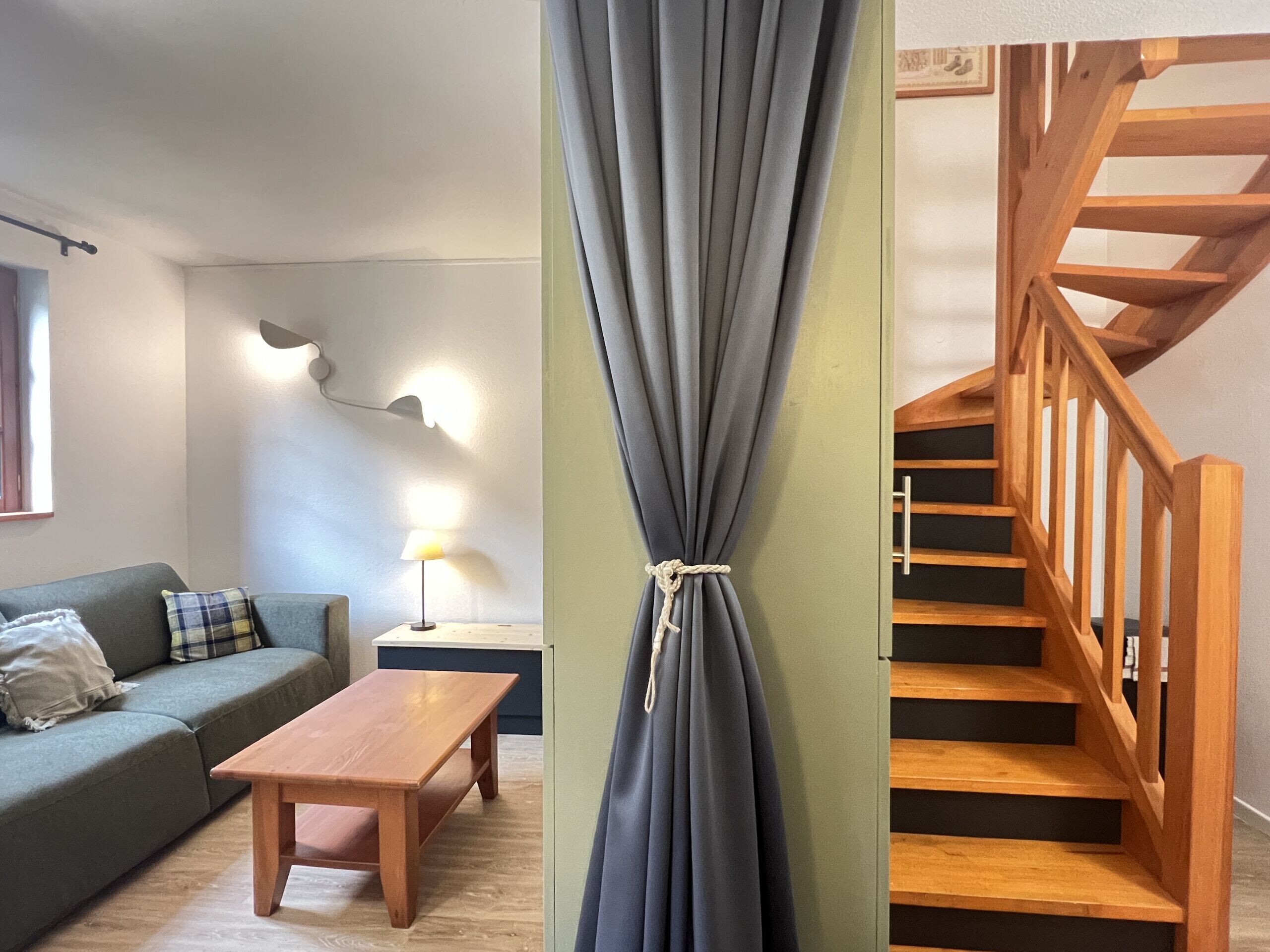 Un salon comprenant un canapé, une table en bois, une lampe et un escalier avec des rampes en bois.