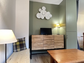 En moderne stue med et træskab, et fladskærms-tv, en lampe og en ternet pude på en sofa.