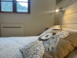 En seng med et strikket tæppe og en pude med et får-motiv.