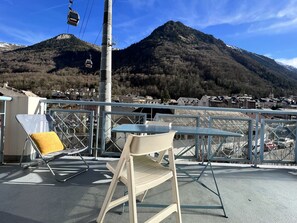 Terraço com mesa e cadeiras, com vista para uma montanha e uma cidade.