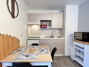 A compact kitchen with a wooden table, a built-in oven, a microwave, and a sink. - -Centre ville, T2 avec terrasse et parking couvert. (Cauterets)
