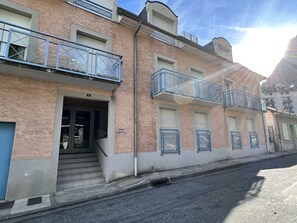 Um edifício de vários andares com fachada de tijolos, várias varandas com grades de metal e um acesso no térreo com degraus que levam a uma porta.