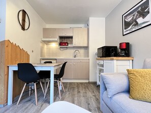 Un espace de vie compact comprenant un coin cuisine, un coin repas et un coin salon avec un canapé et un fauteuil.