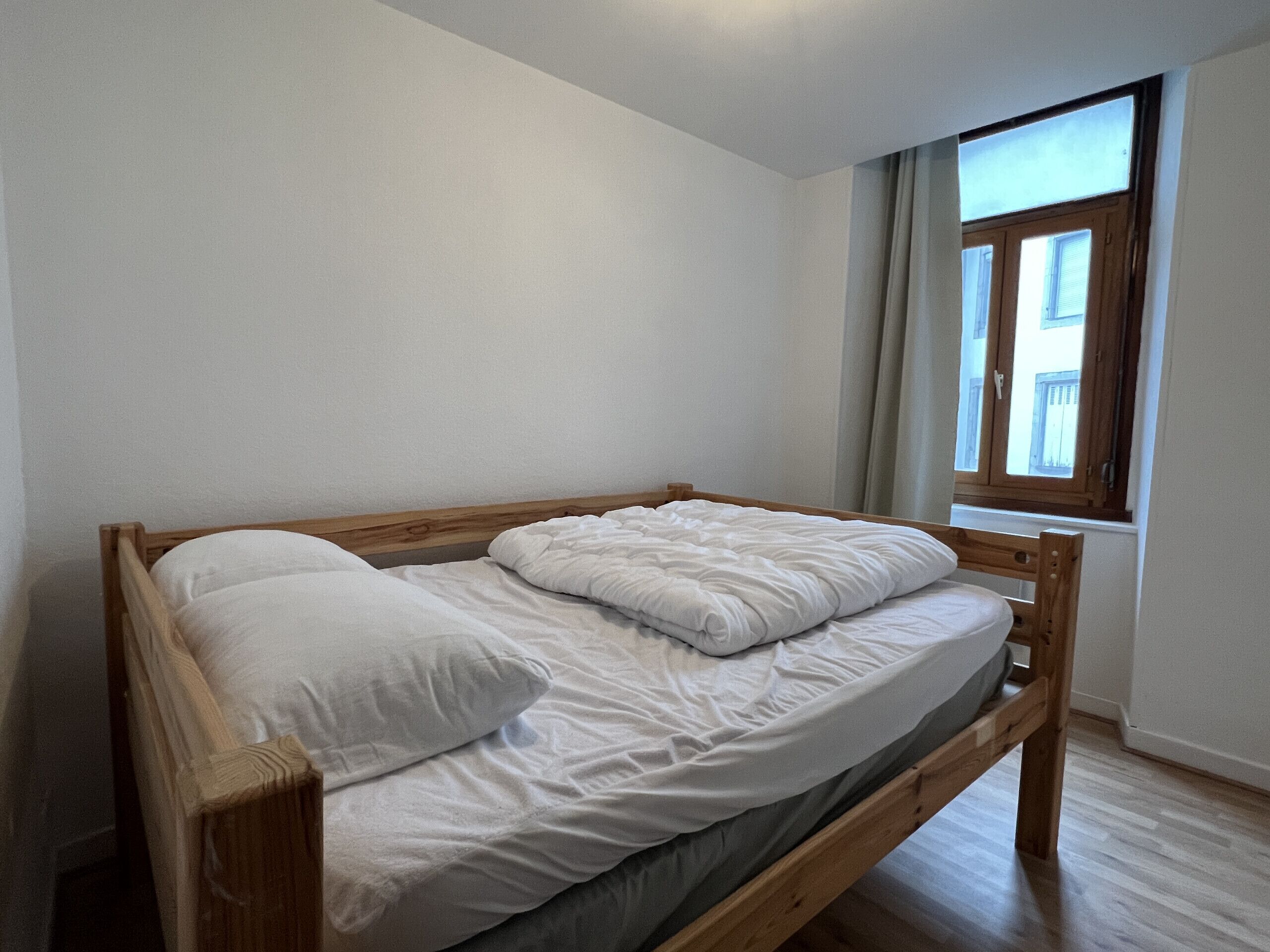 A single bed with a wooden frame and white bedding in a room with a window.