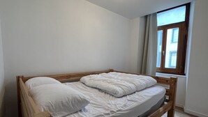 A single bed with wooden headboard and footboard, white bedding, and a window with blinds.