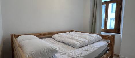 A single bed with a wooden frame and white bedding in a room with a window.