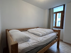 A single bed with wooden headboard and footboard, white bedding, and a window with blinds.