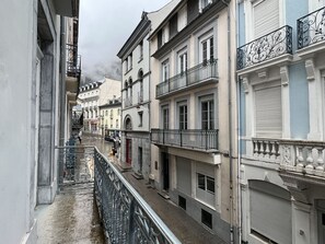 A narrow street with buildings on both sides, featuring balconies with wrought iron railings and shutters on the windows.