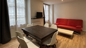 A modern living room with a dark wooden dining table, white chairs, a red sofa, and a television on a black stand.