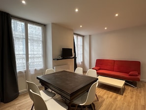A modern living room with a dark wooden dining table, white chairs, a red sofa, and a television on a black stand.