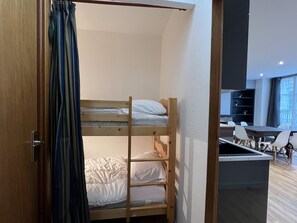 A bunk bed room with a wooden door, a curtain, and a desk area with chairs.