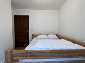 A single bed with a wooden frame and white bedding in a room with white walls and a wooden door.
