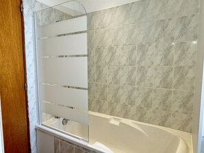 Une salle de bain avec une baignoire, un espace douche et un mur carrelé.