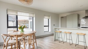 Een moderne keuken met een eetgedeelte, houten vloeren en grote ramen.