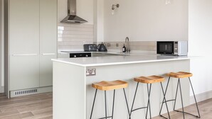 Een moderne keuken met een centraal kookeiland, barstoelen, een magnetron en een roestvrijstalen afzuigkap.