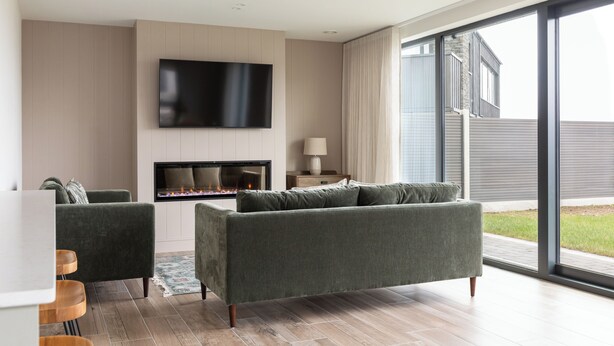 Een moderne woonkamer met een flatscreen-televisie, een open haard en een grote schuifpui naar buiten.
