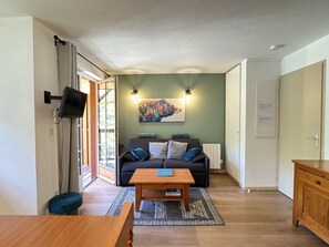 A living room with a sofa, a coffee table, and a TV mounted on the wall. - Duplex 40m2. Balcon. Parking. 5P (Cauterets)