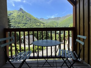 A balcony with a table and two chairs, overlooking a mountainous landscape.