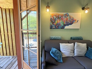 A cozy room with a large window, a colorful abstract painting, and a dark sofa with blue cushions. - Duplex 40m2. Balcon. Parking. 5P (Cauterets)
